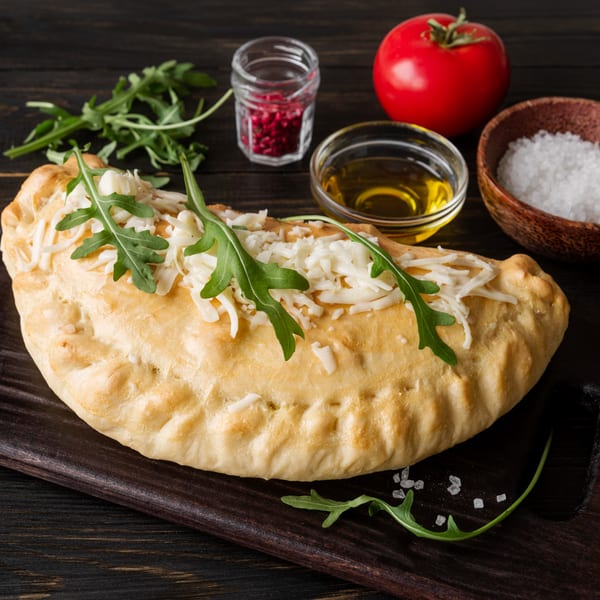 Angelo's Pizza House calzone with cheese and arugula, alongside olive oil, salt, and a tomato.