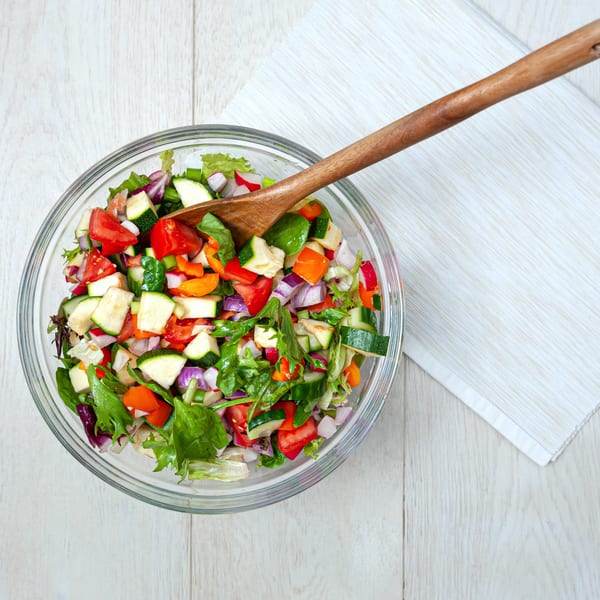 Freshly chopped garden salad with mixed greens, tomatoes, cucumbers, and red onion in a glass bowl.